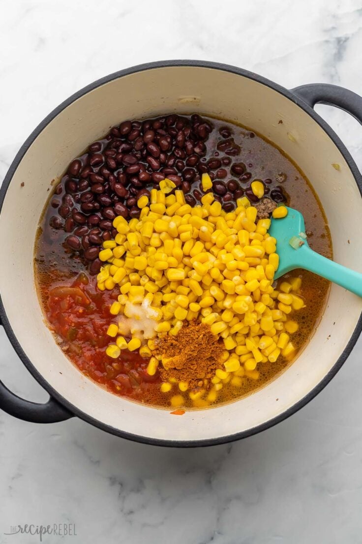 cooked soup ingredients in pot with corn, beans, and spices added on top.