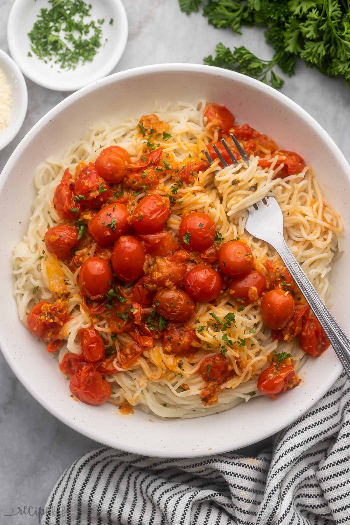 overhead view of a plate full of angel hair pasta and tomatoes with a fork in it.