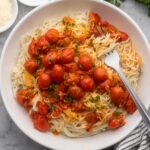 close up of a plate full of angel hair pasta with tomatoes and a fork.