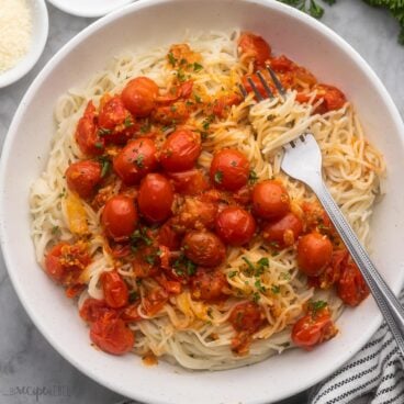 close up of a plate full of angel hair pasta with tomatoes and a fork.