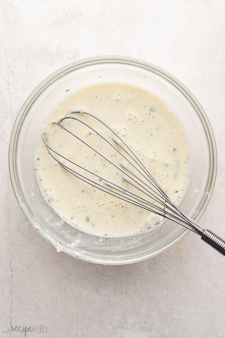 glass mixing bowl with cream mixture and steel whisk.