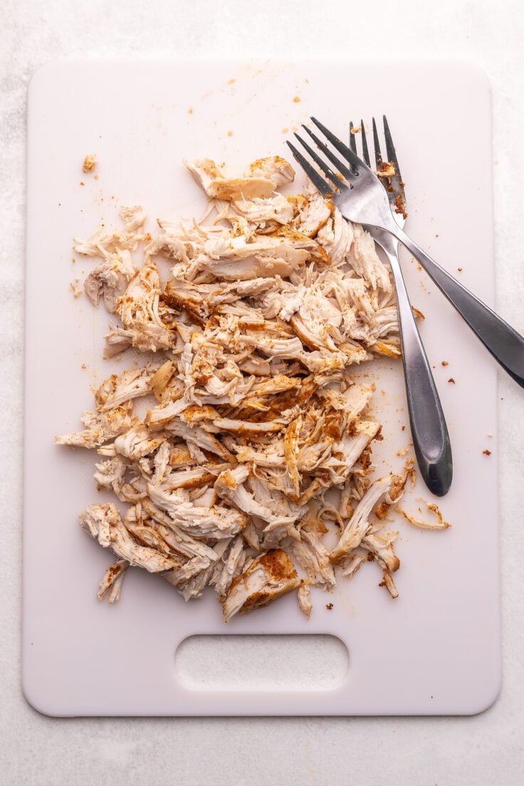 white cutting board with shredded chicken and two forks.