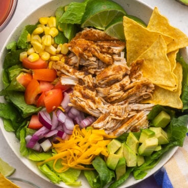 large bowl of chicken taco salad with chips and lime beside.