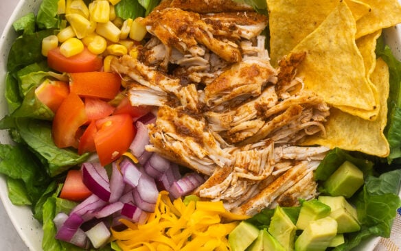 large bowl of chicken taco salad with chips and lime beside.