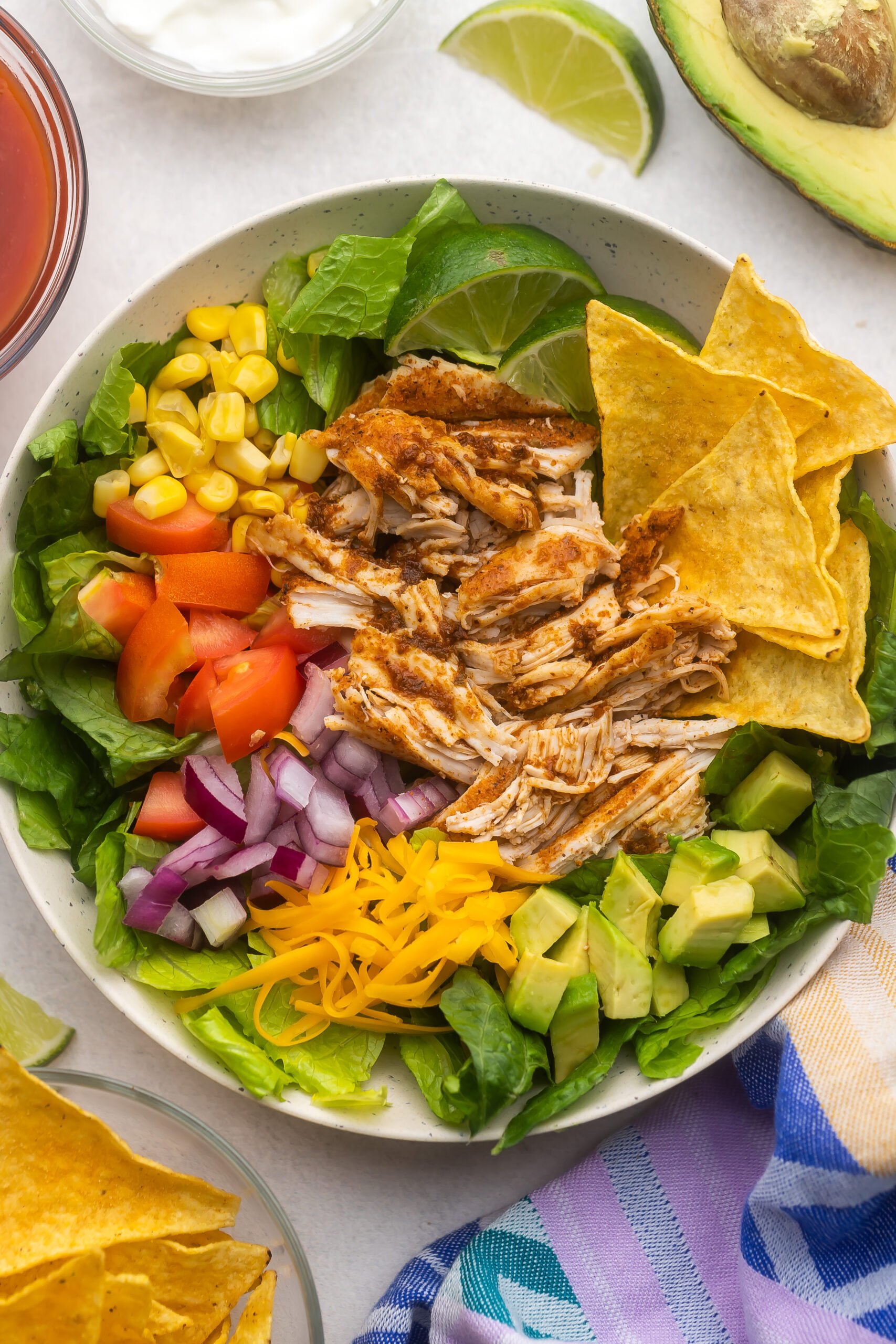 large bowl of chicken taco salad with chips and lime beside.