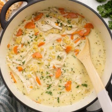 creamy chicken noodle soup in pot with wooden spoon.