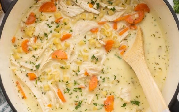 creamy chicken noodle soup in pot with wooden spoon.