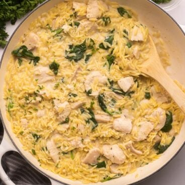 white pan filled with creamy chicken orzo and parsley beside.