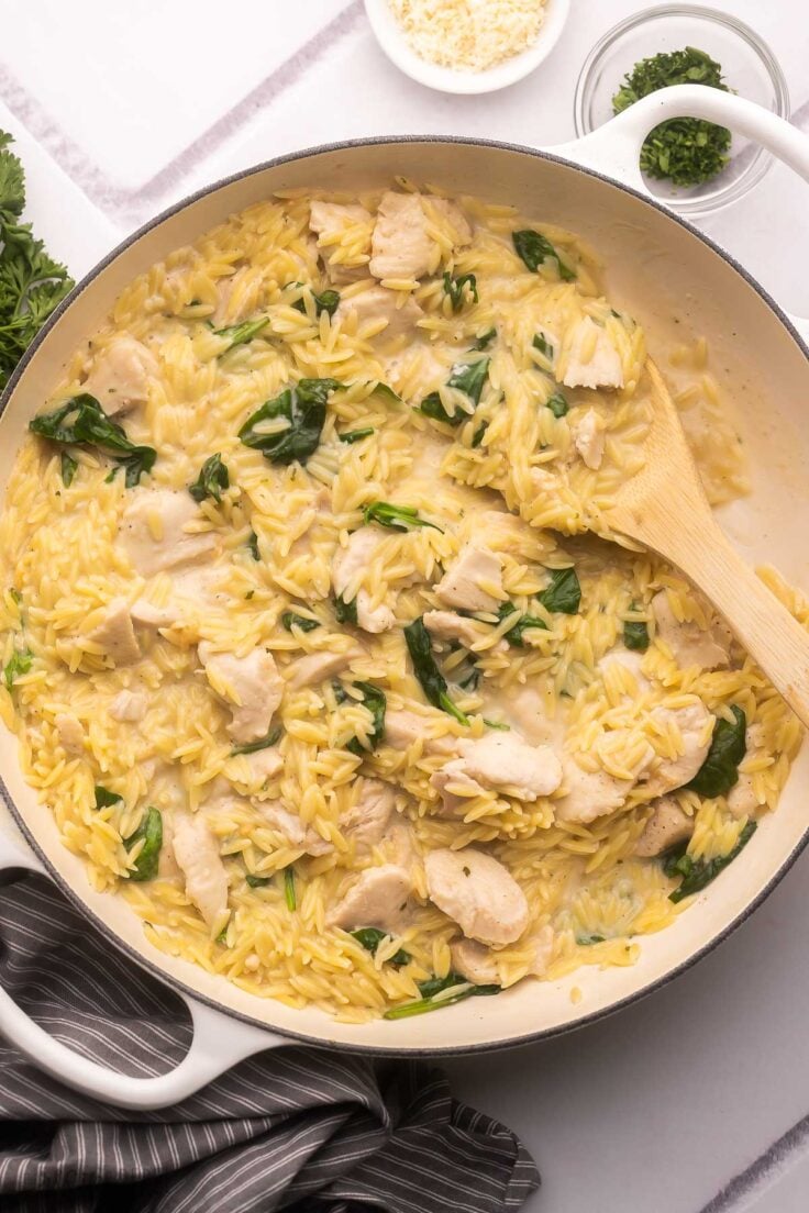 large pan filled with creamy chicken orzo and wooden ladle.