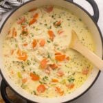 close up of a large pot of creamy chicken rice soup with wooden spoon.