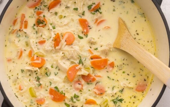 close up of a large pot of creamy chicken rice soup with wooden spoon.