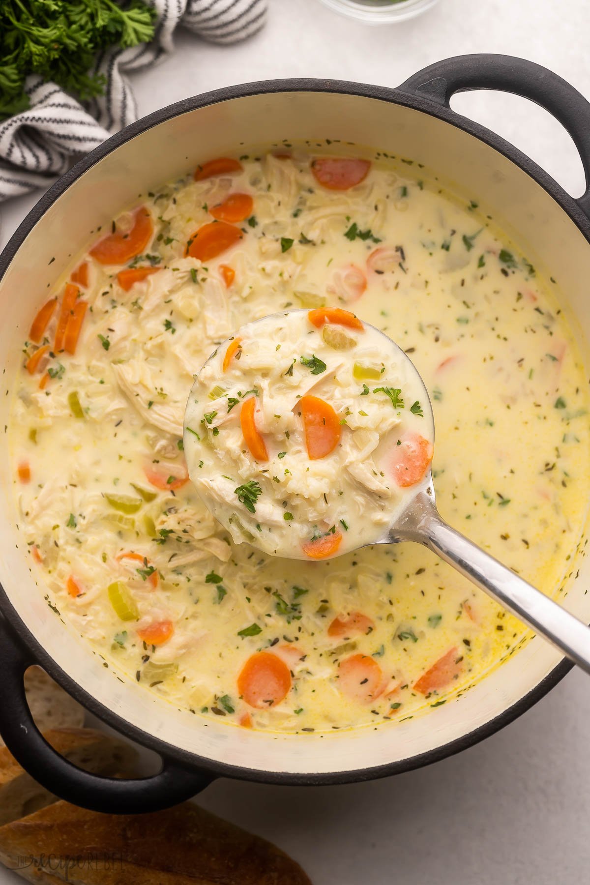 steel ladle scooping creamy chicken rice soup out of large pot.