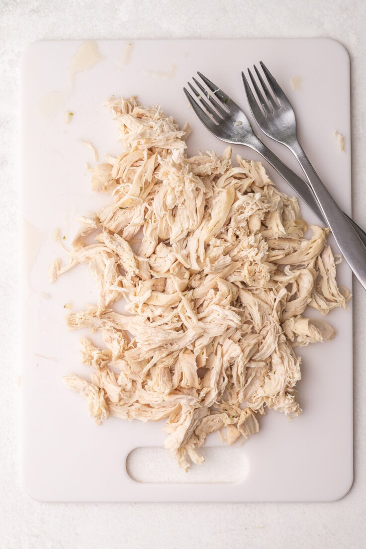 shredded chicken on a white cutting board with two forks.