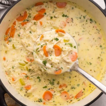 steel ladle scooping creamy chicken rice soup out of large pot.