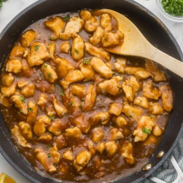 orange chicken in large pan with parsley and orange slices beside.