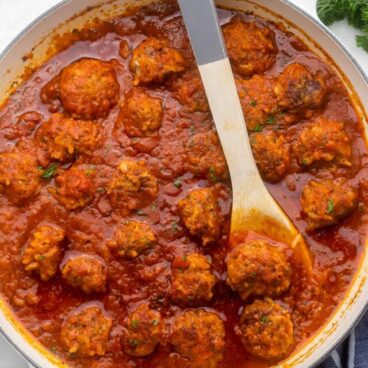 wooden spoon in pan of porcupine meatballs with parsley beside.
