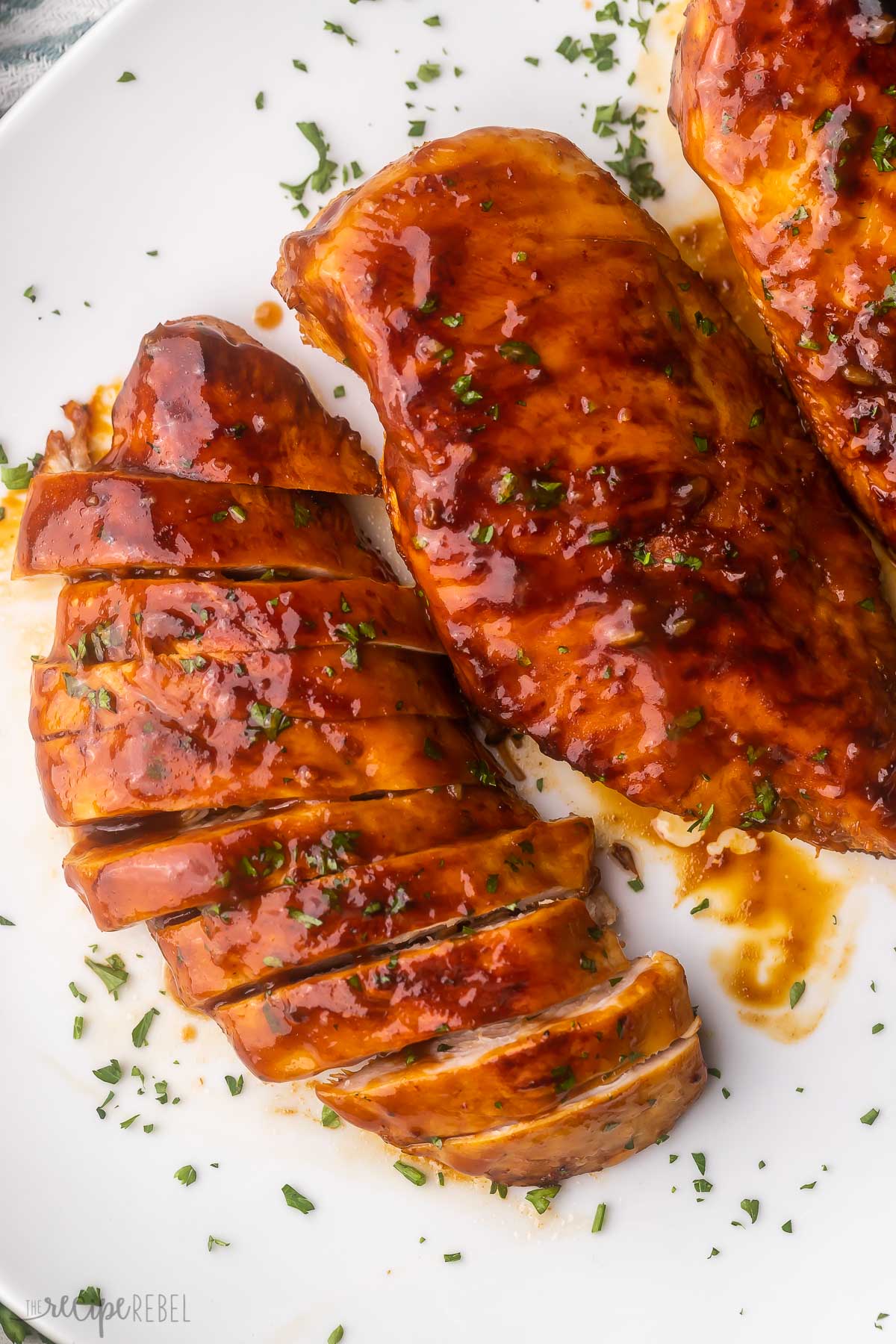 chicken breasts on a white plate topped with chopped parsley.