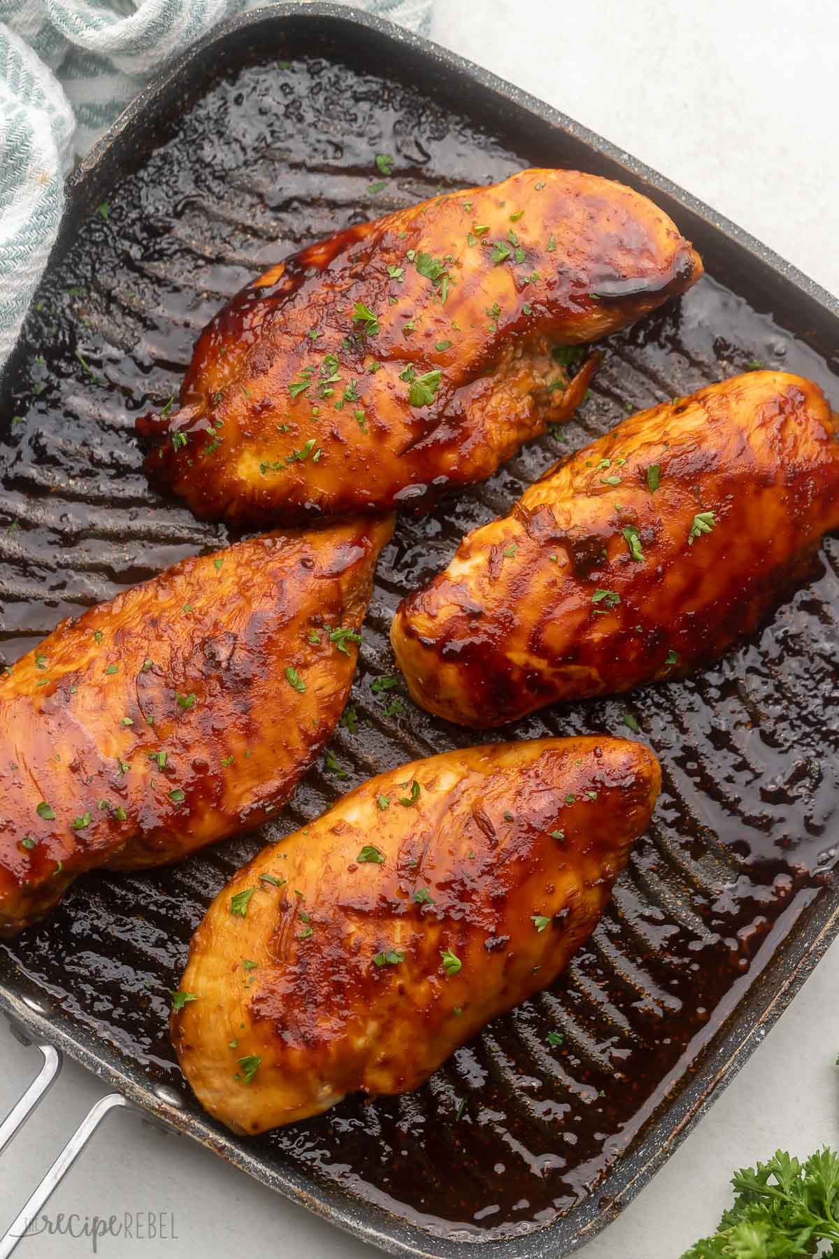 four grilled chicken breasts in black pan.