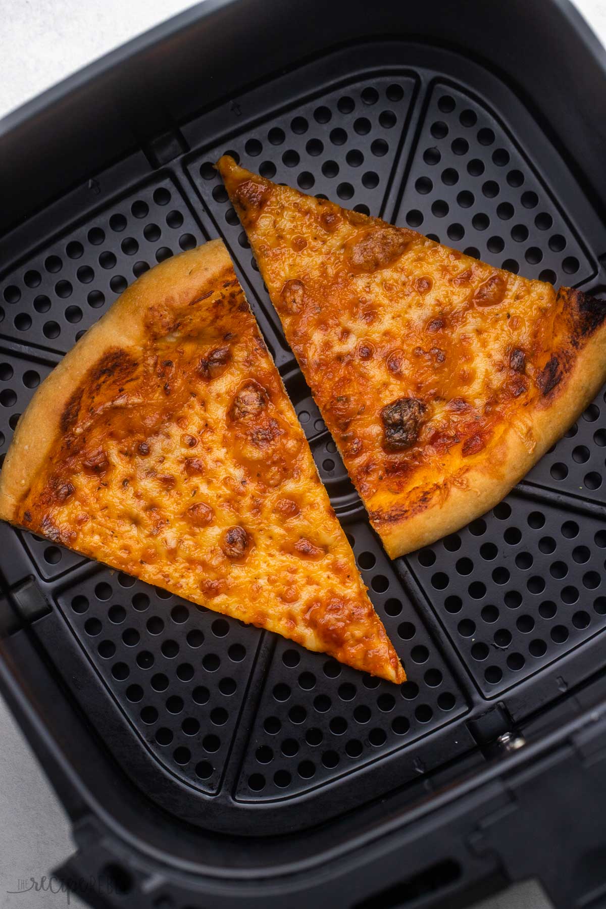 two slices of cheese pizza in air fryer basket.
