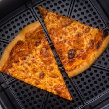 close up of two slices of cheese pizza in air fryer basket.