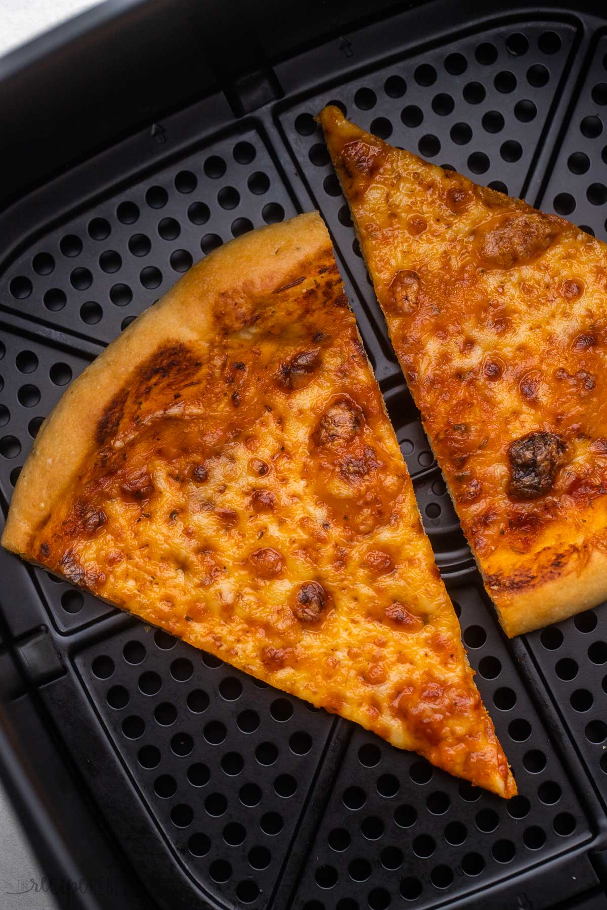 two slices of cheese pizza in black air fryer basket.