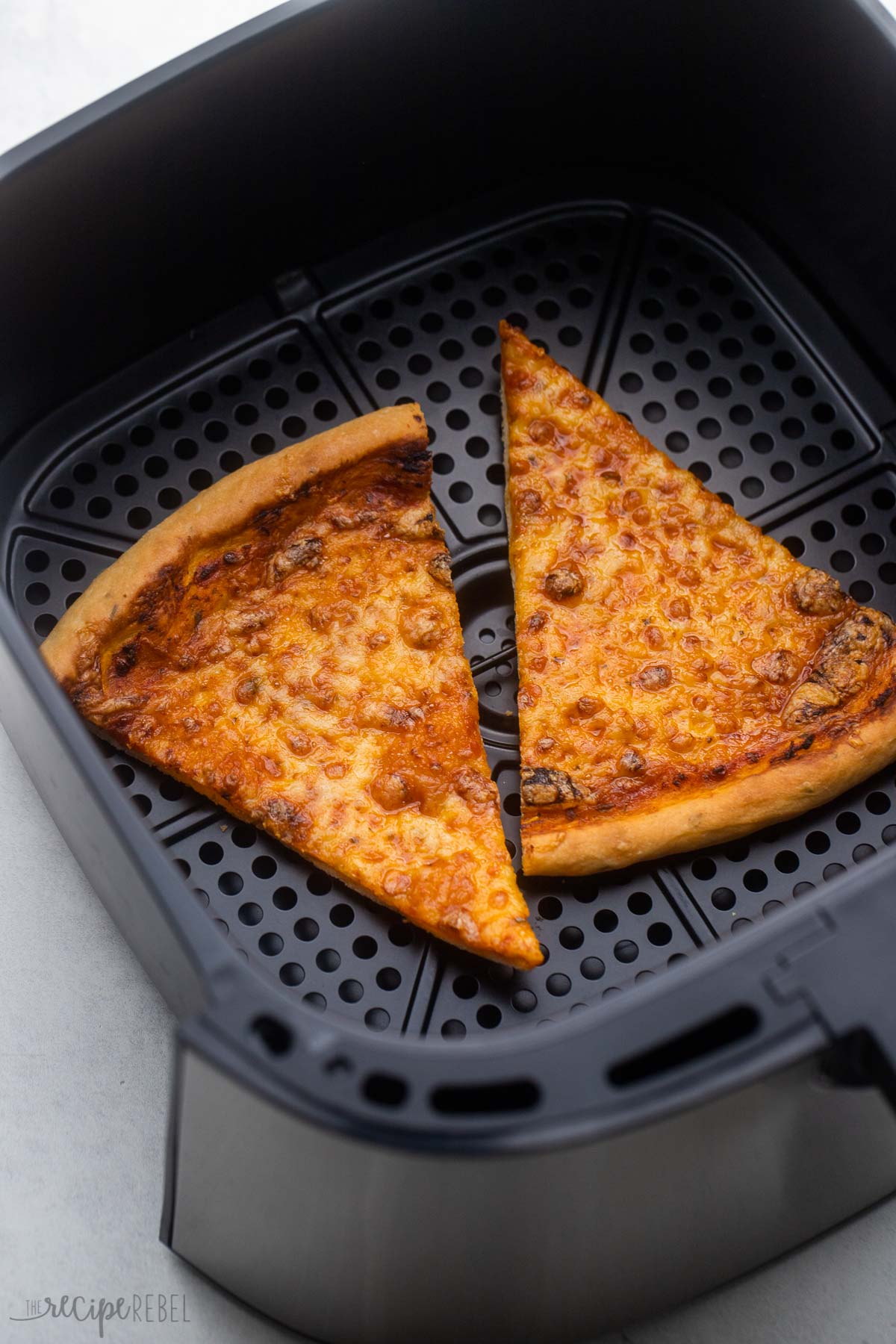 two slices of cheese pizza in air fryer basket on grey surface.
