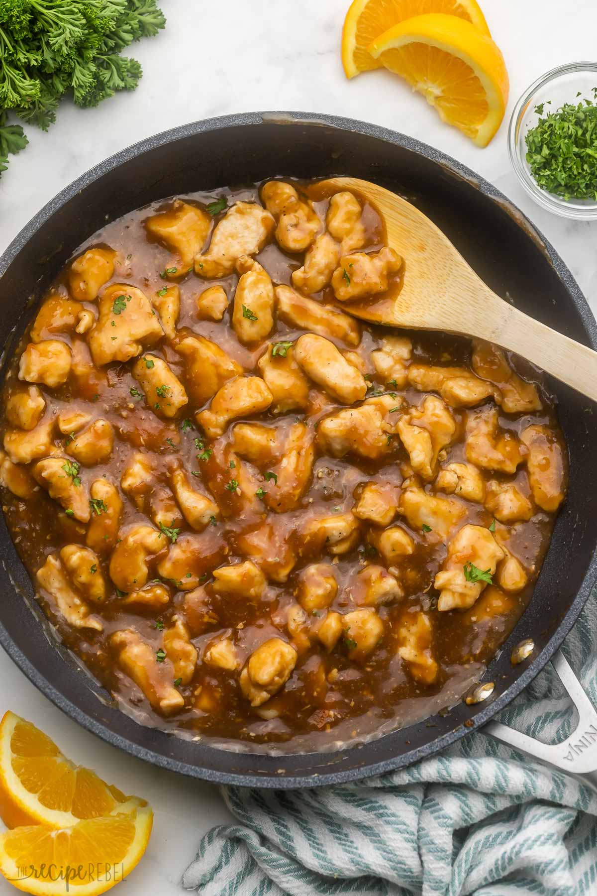 orange chicken in large pan with parsley and orange slices beside.