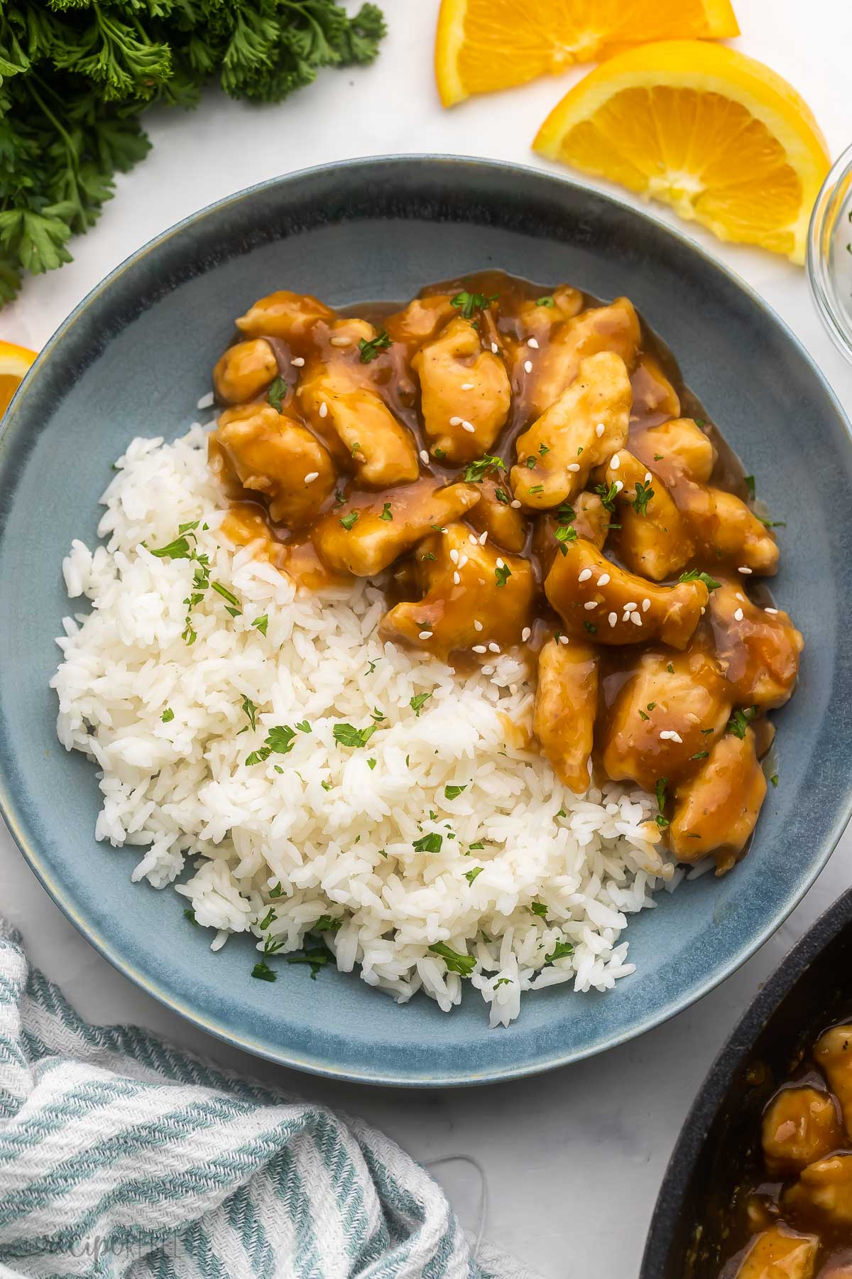 blue bowl filled with orange chicken and rice with orange slices beside.