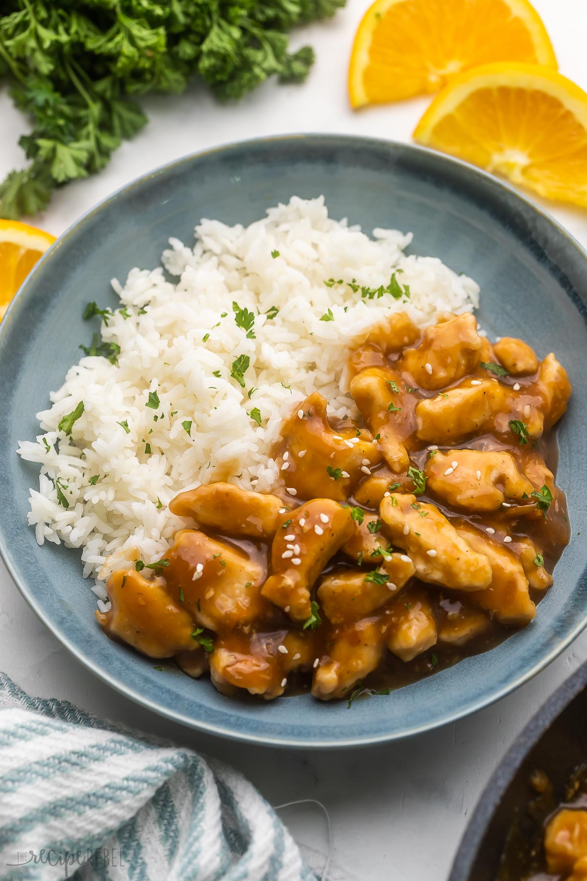 white rice and orange chicken in a blue bowl with sesame seeds on top.