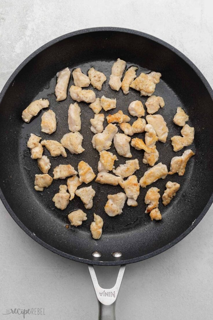 black pan on grey surface with cooked pieces of chicken.