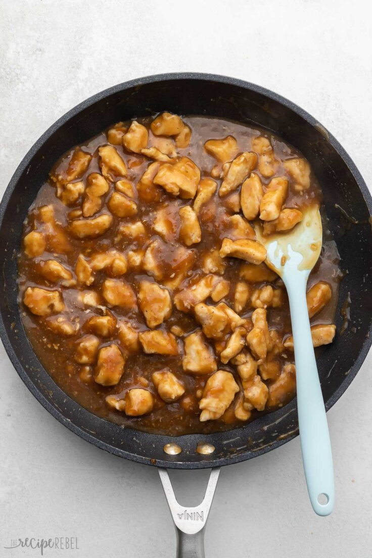 cooked chicken and sauce in black frying pan with blue spatula.