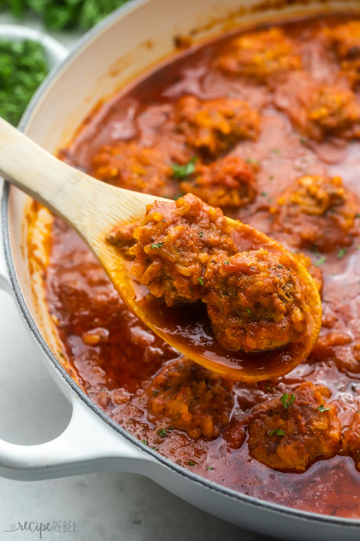 Porcupine Meatballs are homemade beef meatballs that are boldly seasoned, cooked in a rich tomato sauce, and have plenty of "spikes" from the addition of white rice! They're so easy to whip up with just about 15 minutes of prep time. #meatball #groundbeef #dinner #recipe | dinner recipes | dinner ideas | ground beef recipes | meatball recipes | gluten free | rice | wooden spoon scooping porcupine meatballs out of pan.