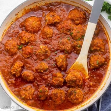 large pan full of porcupine meatballs with wooden spoon and topped with chopped parsley.