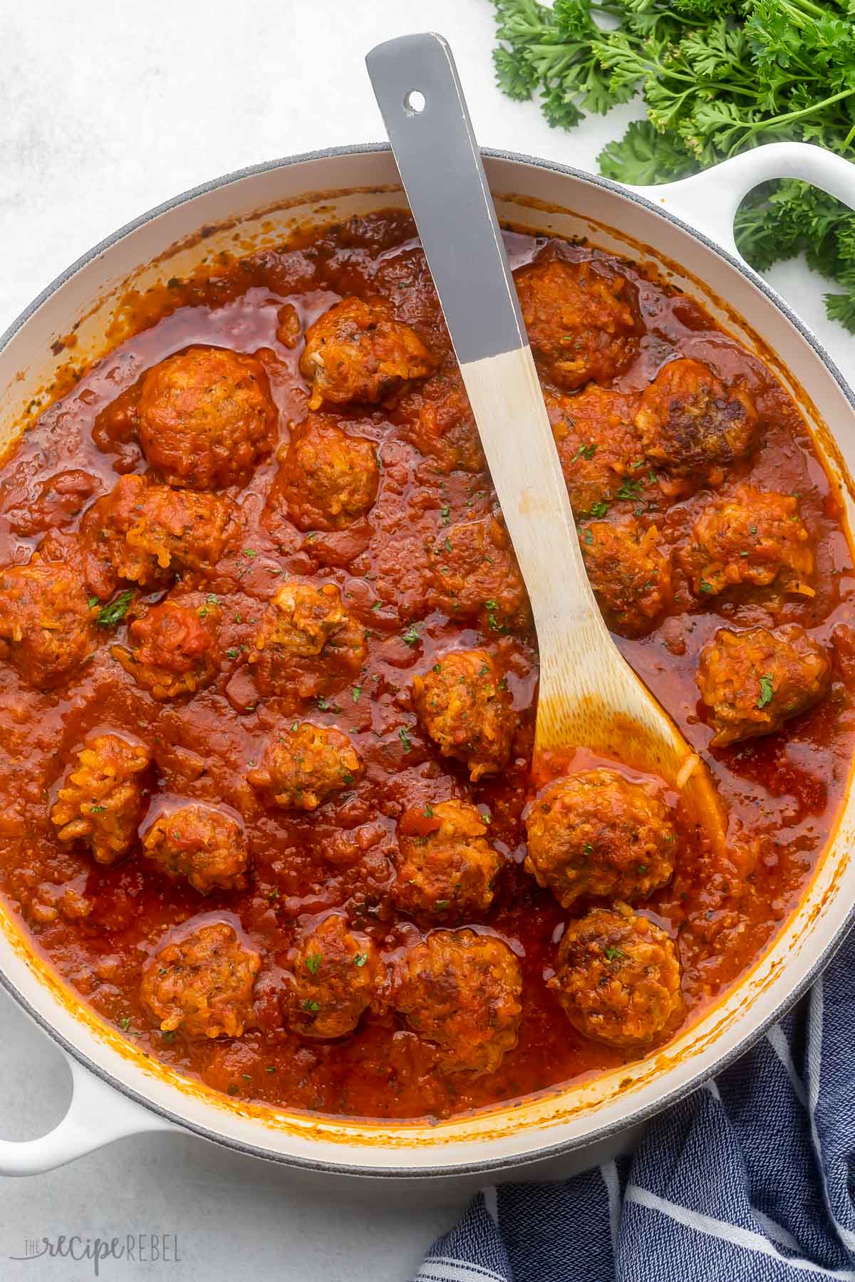 wooden spoon in pan of porcupine meatballs with parsley beside.