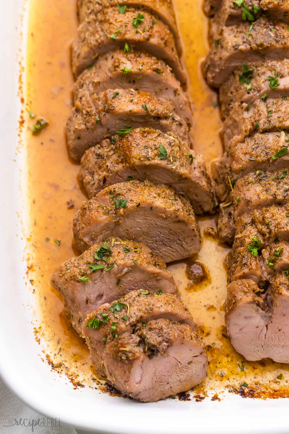 sliced pork tenderloin in white baking dish topped with chopped parsley.