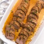 sliced pork tenderloin in white baking dish topped with chopped parsley.