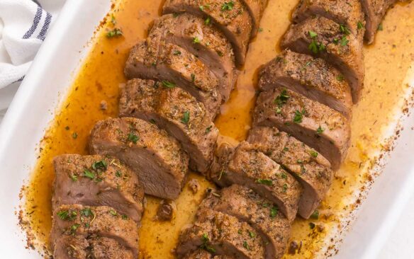 sliced pork tenderloin in white baking dish topped with chopped parsley.