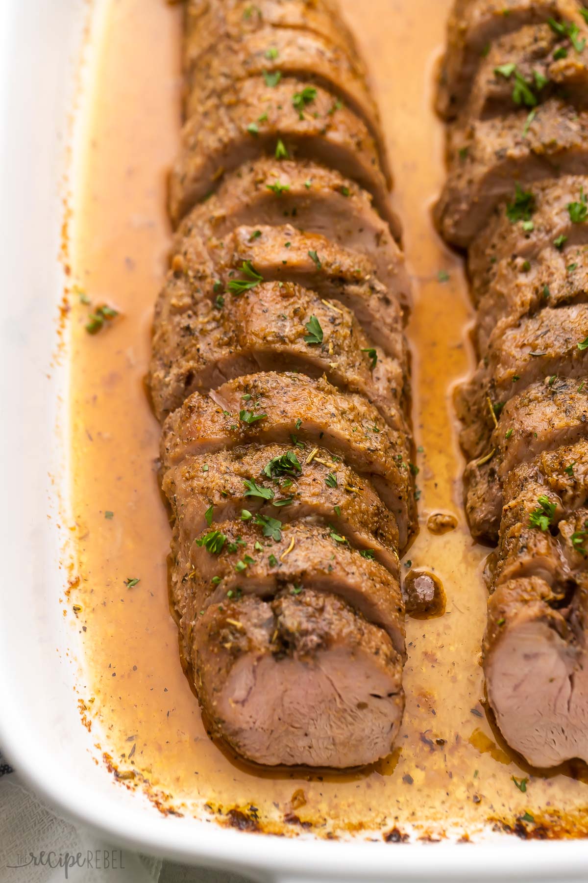 sliced roast pork tenderloin in white baking dish.