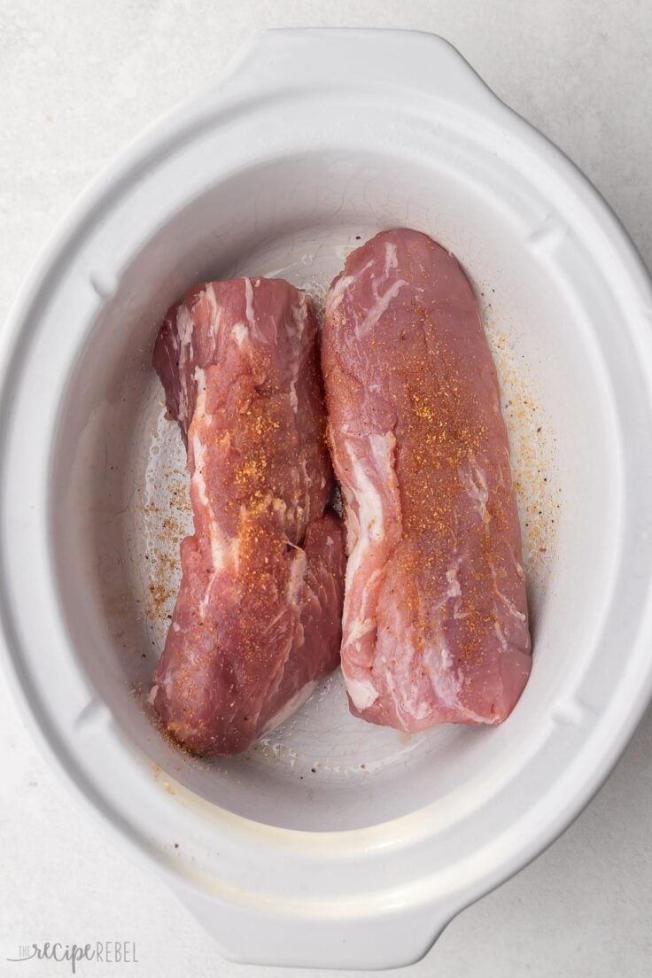 pork tenderloin in white slow cooker with seasonings on top.