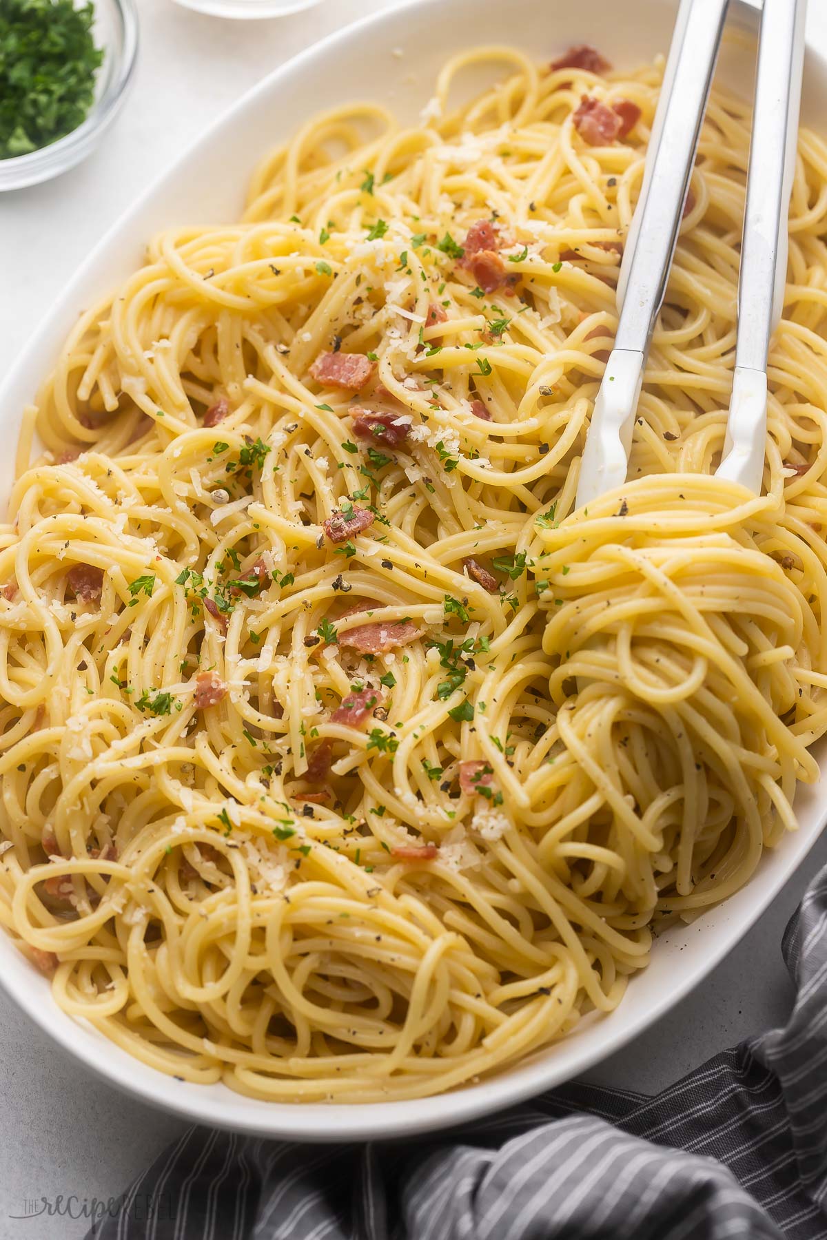 large white dish full of spaghetti carbonara topped with chopped parsley.