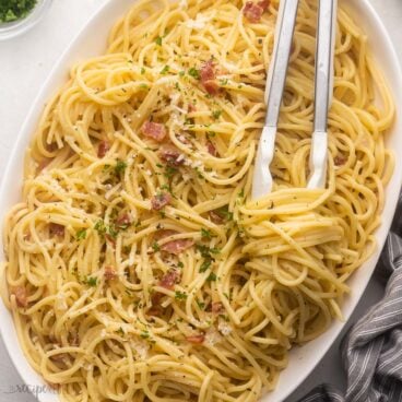 close up of tongs in a large dish of spaghetti carbonara.