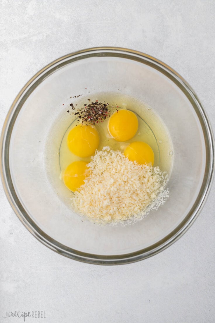 glass mixing bowl with eggs, parmesan and black pepper.