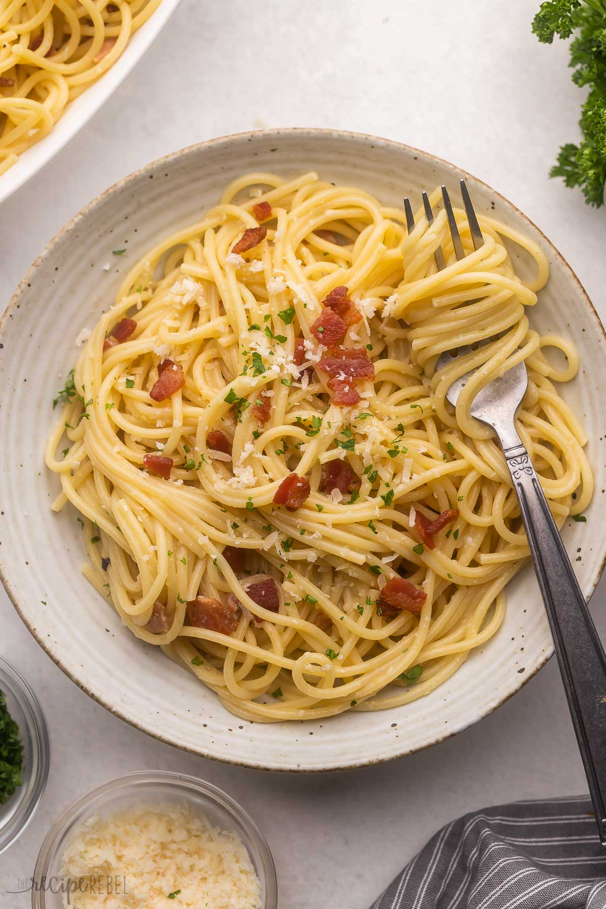 grey plate full of spaghetti carbonara topped with bacon bits.