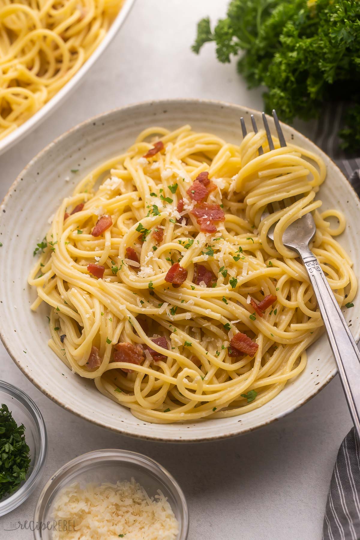 large plate full of spaghetti carbonara with parsley and parmesan beside.