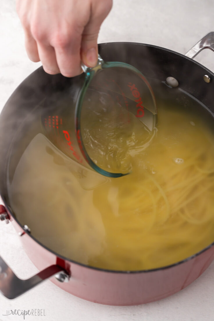 measuring cup scooping pasta water out of red pot.