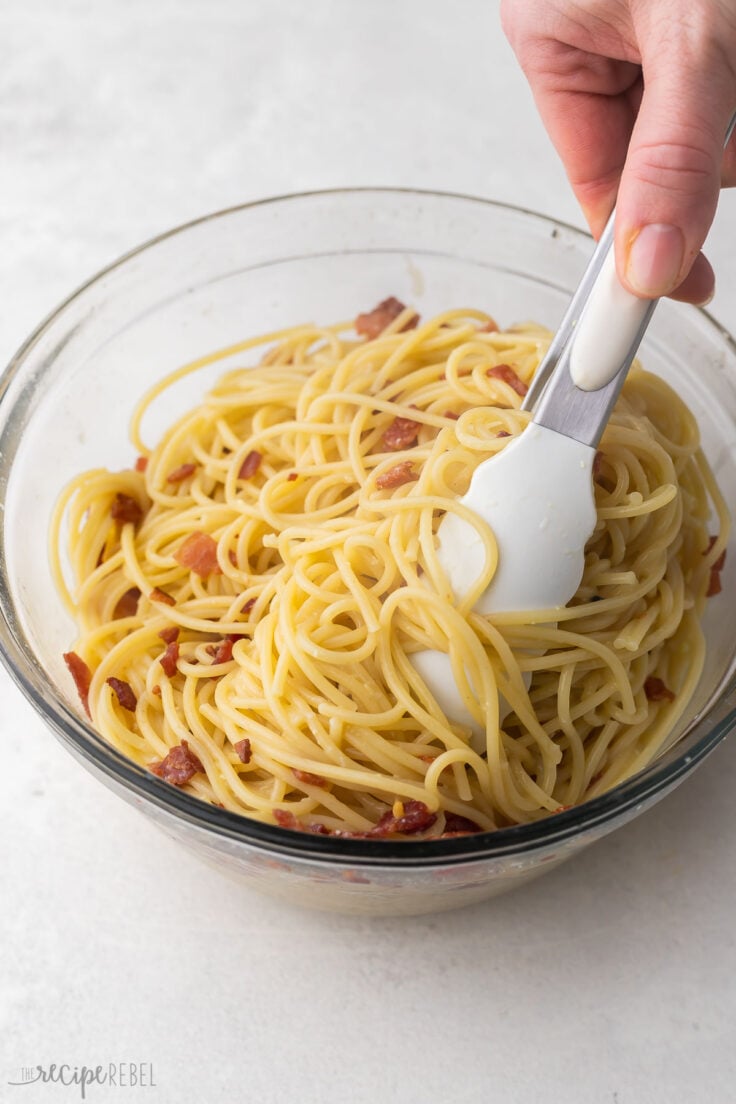 glass bowl filled with spaghetti carbonara and tongs in it.