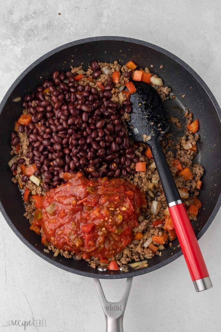 salsa and beans added to ingredients in black frying pan.