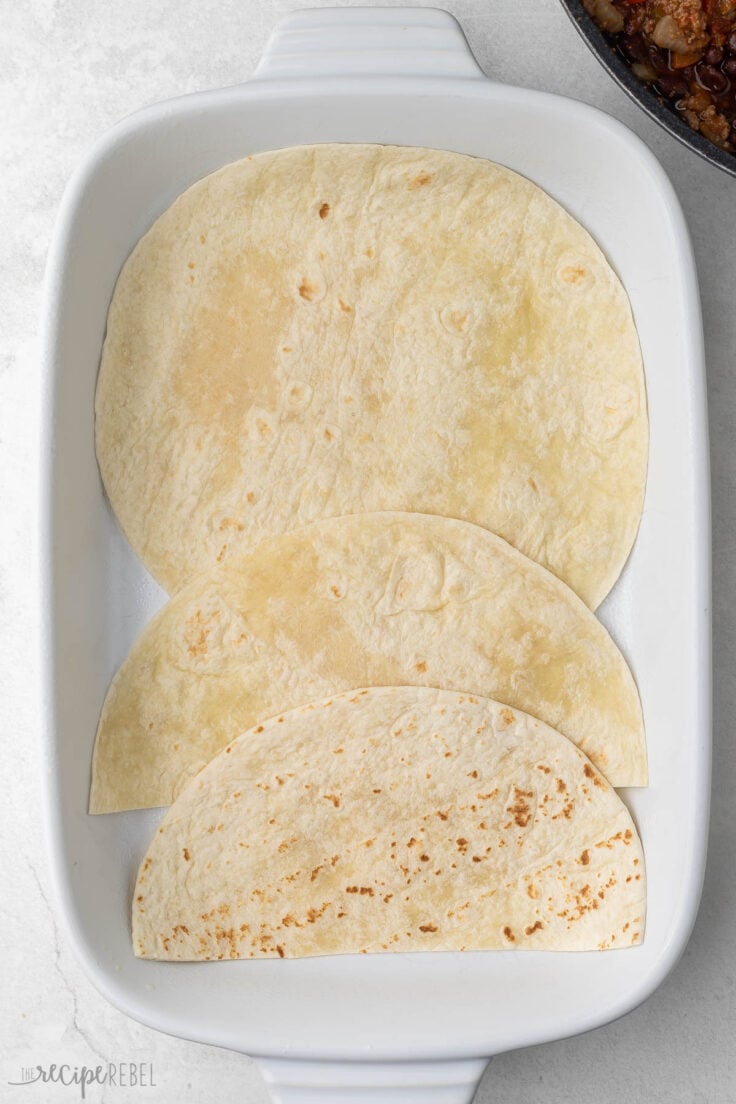 tortillas lying in a white baking dish.