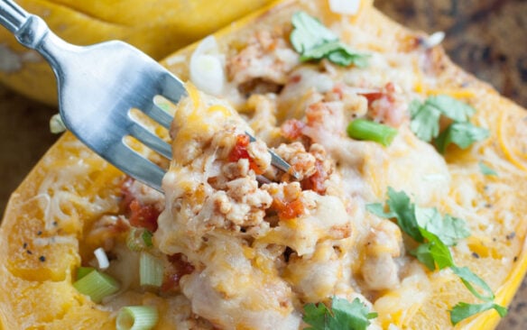 A fork is lifting a bite of chicken taco spaghetti squash from the squash.