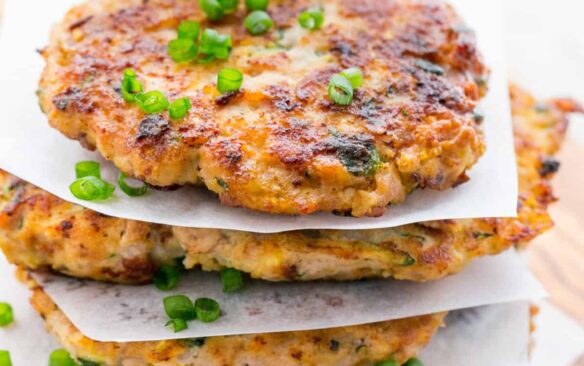 A stack of chicken zucchini fritters are placed on a wooden surface.